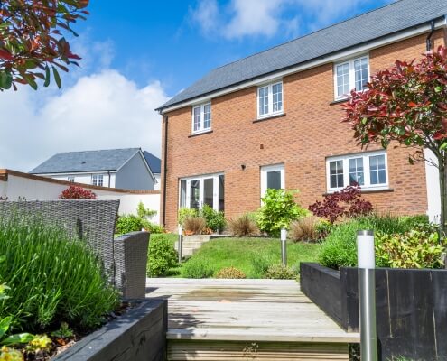 Rear garden with flower beds and the rear of a red brick house