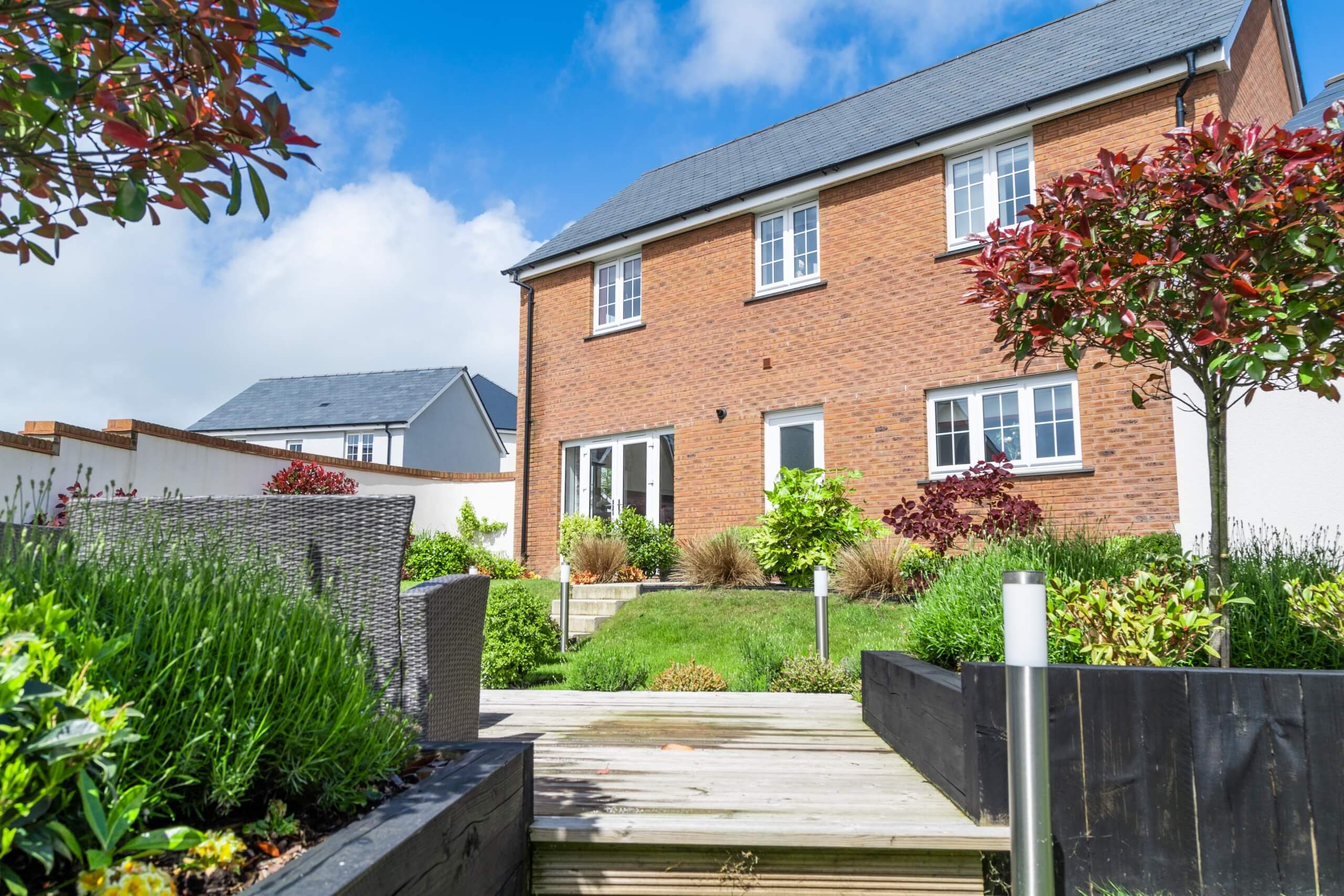 Rear garden with flower beds and the rear of a red brick house